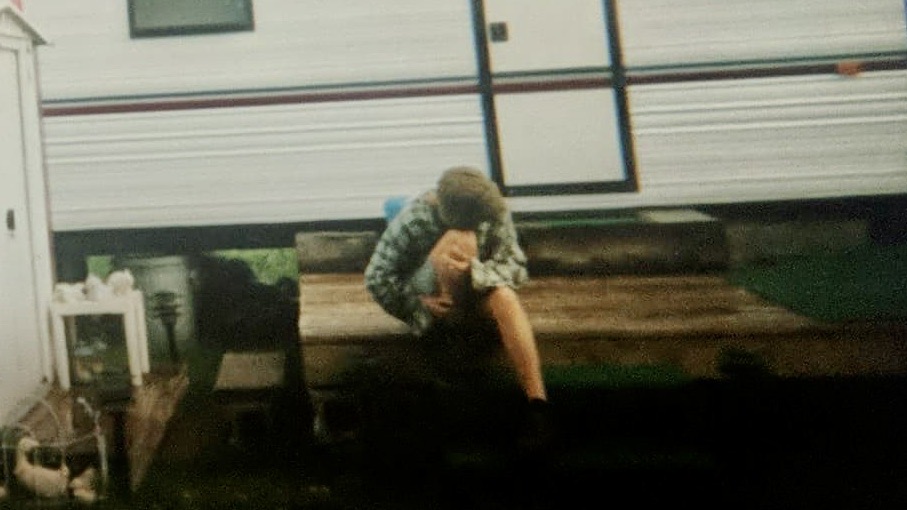 woman in a hat on a small porch in front of a mobile home