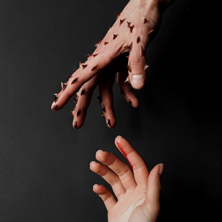 hand of man covered with thorns and bleeding finger of woman hand