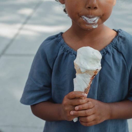 little child with dirty mouth standing with ice cream on street