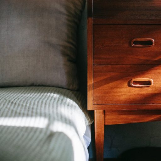 comfortable bed located near wooden night stand in sun rays